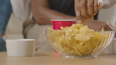 Couple-Sitting-On-Sofa-At-Home-Eating-Chips-And-Dips-Watching-TV-Together