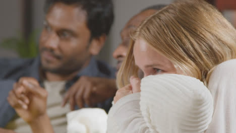 Multi-Cultural-Friends-Sitting-On-Sofa-At-Home-Watching-TV-Horror-Movie-And-Eating-Popcorn-1