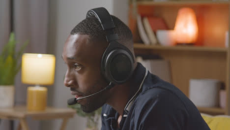 Man-Wearing-Headset-Sitting-On-Sofa-At-Home-Gaming-Online
