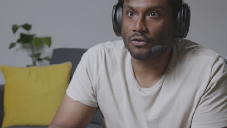 Man-Wearing-Headset-Sitting-On-Sofa-At-Home-Gaming-Online-7