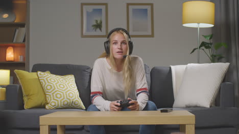 Woman-Wearing-Headset-Sitting-On-Sofa-At-Home-Gaming-Online-5