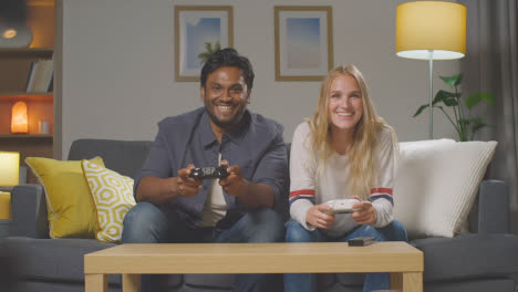 Multi-Cultural-Friends-Or-Couple-Sitting-On-Sofa-At-Home-Gaming-Online-3