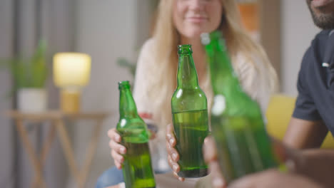 Multi-Cultural-Friends-Sitting-On-Sofa-At-Home-Talking-Drinking-Beer-And-Doing-Cheers