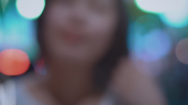 Coming-to-Focus-Portrait-of-the-Beautiful-Alternative-East-Asian-Girl-Smiling-on-Camera.-In-the-Background-Blurred-Big-City-Lights-Glowing.