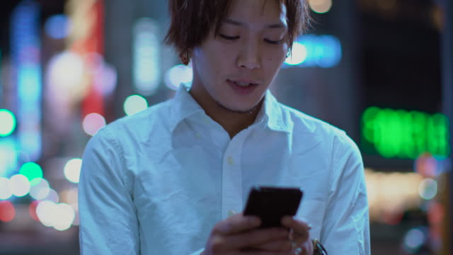Porträt-der-schönen-japanischen-Alternative-Junge-mit-Handy.-Im-Hintergrund-Plakate-Großstadt-Werbung-Lichter-leuchten-in-der-Nacht.