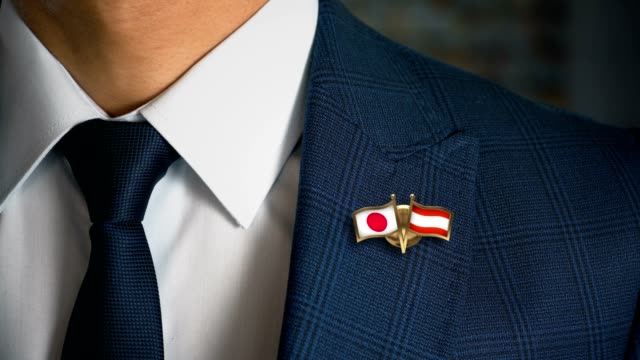 Empresario-caminando-hacia-cámara-con-amigo-país-banderas-Pin-Japón---Austria
