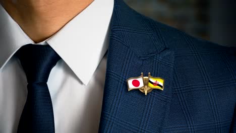 Businessman-Walking-Towards-Camera-With-Friend-Country-Flags-Pin-Japan---Brunei