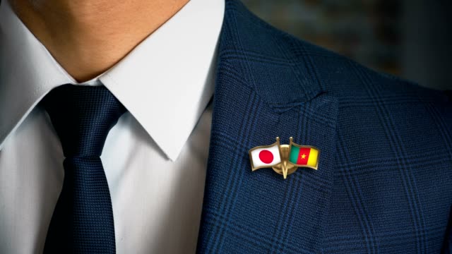 Businessman-Walking-Towards-Camera-With-Friend-Country-Flags-Pin-Japan---Cameroon