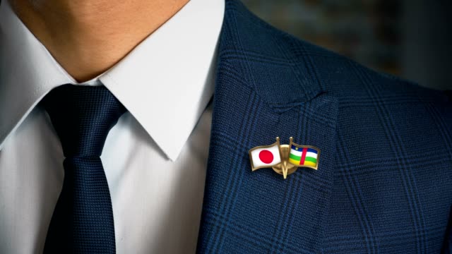Businessman-Walking-Towards-Camera-With-Friend-Country-Flags-Pin-Japan---Central-African-Republic