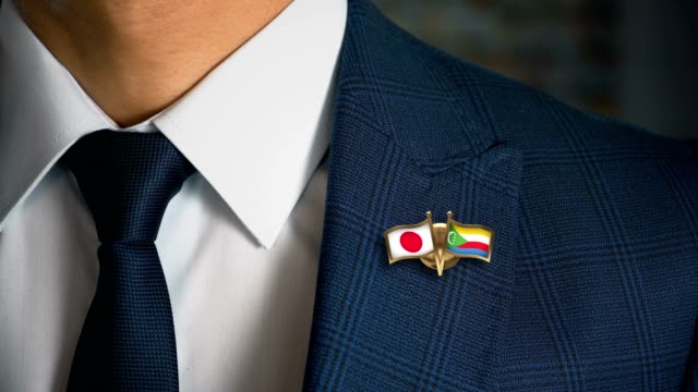Businessman-Walking-Towards-Camera-With-Friend-Country-Flags-Pin-Japan---Comoros