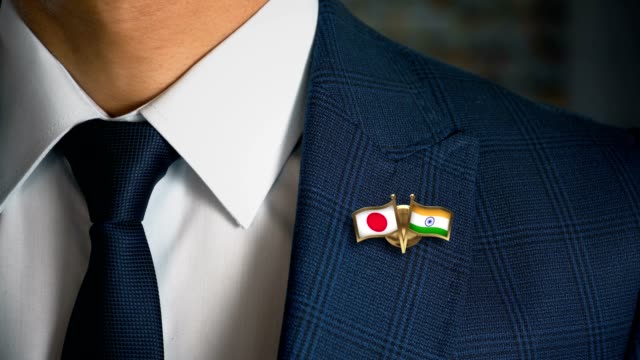Empresario-caminando-hacia-cámara-con-amigo-país-banderas-Pin-Japón---India