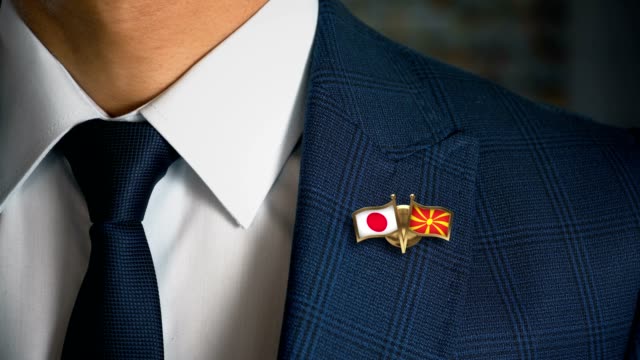 Businessman-Walking-Towards-Camera-With-Friend-Country-Flags-Pin-Japan---Macedonia
