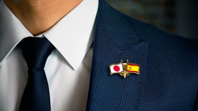 Businessman-Walking-Towards-Camera-With-Friend-Country-Flags-Pin-Japan---Spain