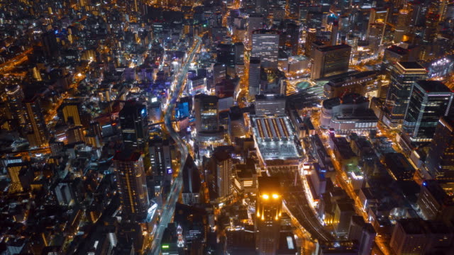 Aerial-night-hyper-lapse-over-Osaka-city-Japan-with-Umeda(Osaka)-train-station-and-many-skyscraper-building-and-vehicles-transporting-along-the-road.
