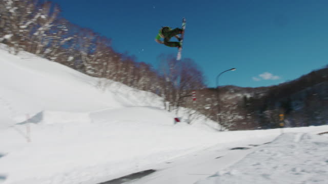 Snowboarder-salta-sobre-el-camino-mientras-se-hace-girar-un-truco-Freestyle-en-un-día-soleado-de-invierno