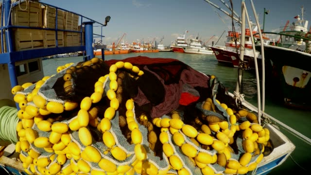 Schleppnetz-Fischernetz-mit-gelben-Schwimmern-liegt-auf-dem-Boot,-Schiffe-an-der-Pier-in-der-Ferne