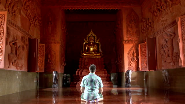 Ein-Mann-betet-kniend-vor-einer-Buddhastatue-in-einem-buddhistischen-Tempel