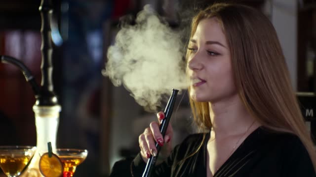 Girls-are-in-a-bar-in-the-evening,-smoke-a-hookah,-drink-cocktails-and-speak-with-each-other-in-slow-motion-in-4k-resolution