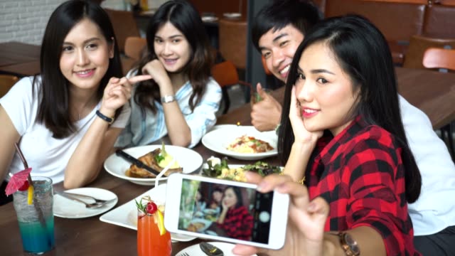 Young-Asian-people-taking-selfie-photos-and-having-lunch-together-at-restaurant-while-they-keep-changing-poses