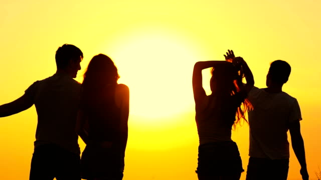 Die-Silhouetten-der-tanzenden-Menschen-auf-dem-Hintergrund-des-Sonnenaufgangs.-Slow-motion