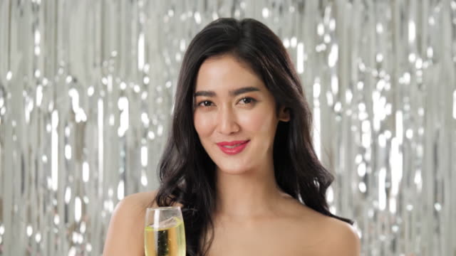 Schöne-asiatische-Frau-mit-Glas-Champagner-tanzen-unter-Konfetti-über-Silber-Glitzer-Hintergrund,-Slow-motion