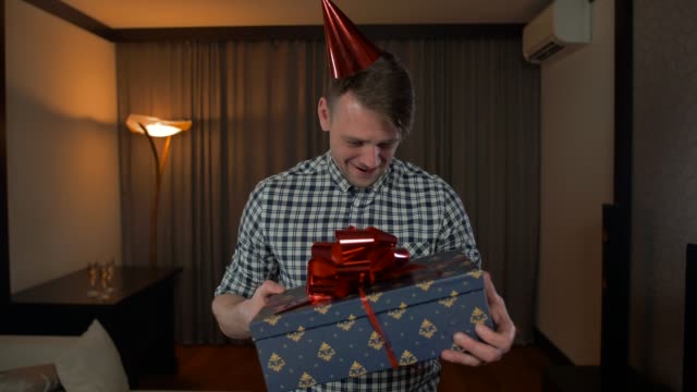 POV-Attractive-male-getting-birthday-present-box-with-big-red-bow-in-cozy-house-living-room