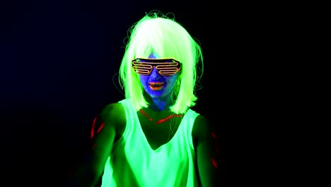 Woman-with-UV-face-paint,-wig,-glowing-clothing-dancing-in-front-of-camera.-Caucasian-woman.-.