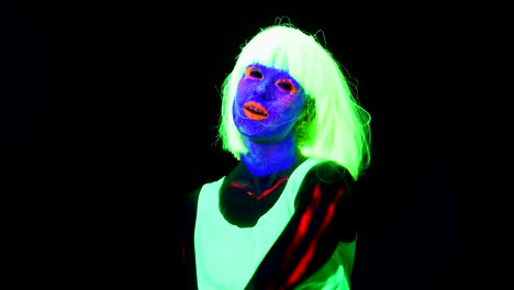 Woman-with-UV-face-paint,-wig,-glowing-clothing-dancing-in-front-of-camera-and-shaking-head,-shoulder-shot.-Caucasian-woman.-.