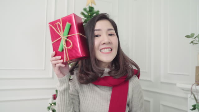 Alegre-feliz-joven-mujer-asiática-con-regalos-de-Navidad-sonriendo-a-la-cámara-en-su-sala-de-estar-en-el-país-en-el-Festival-de-Navidad.-Mujer-de-estilo-de-vida-celebrar-Navidad-y-año-nuevo-concepto.