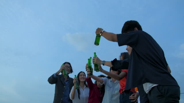 Group-of-young-friends-dancing-and-having-fun-celebrate-with-toast-and-clinking-raising-glasses-at-summer-rooftop-party.-Slow-Motion.