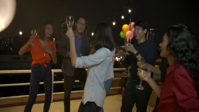 Group-of-young-friends-dancing-and-having-fun-celebrating-New-Year-and-Christmas-Festival-together-at-summer-rooftop-party.-Slow-motion.