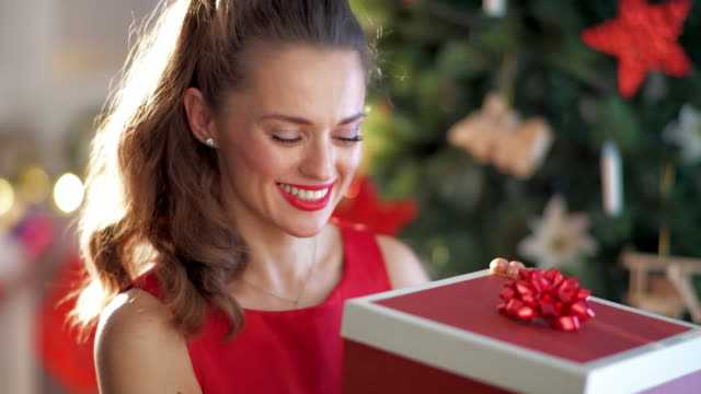 glückliche-junge-Frau-Weihnachtsbaum-Weihnachtsgeschenk-öffnen