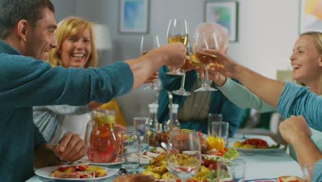 Große-Familie-und-Freunde-feiern-zu-Hause,-vielfältige-Gruppe-von-Menschen-versammelten-sich-am-Tisch-anstoßen-in-einem-Toast.-Leute-Essen,-trinken-und-Spaß-haben.-Tagsüber-Festlichkeit-im-Wohnzimmer.