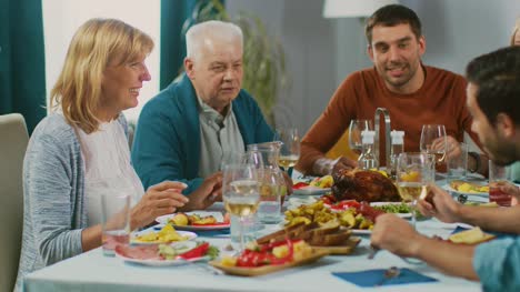 Familiares-y-amigos-en-la-mesa-del-comedor.-Senior-pareja-hablando,-bromeando-y-comer.-Viejas-y-jóvenes-personas-riendo-divertido.
