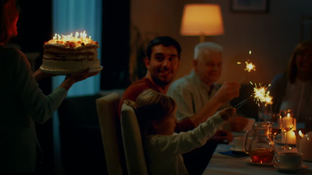 Following-Shot-of-a-Daughter-Bringing-Birtday-Cake-with-Candlelights-to-Her-Senior-Mother.-Family-Dinner-and-Celebration,-People-Gathered-at-the-Evening-Dinner-Table.