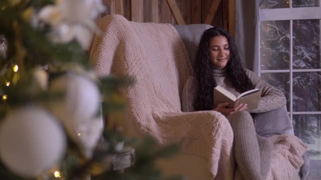 A-young-girl-sits-in-a-chair-near-the-Christmas-tree-and-reads-a-book