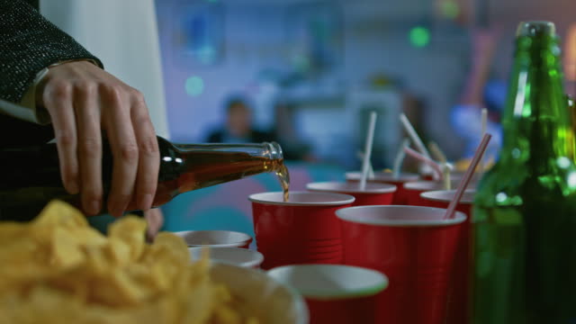 Auf-der-wilden-Party:-Person-in-rote-Tasse-trinken-aus-einer-Flasche-ergießt.-Im-Hintergrund-unscharf-tanzen-Menschen.