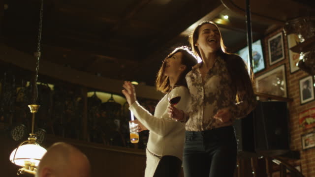 Zwei-Mädchen-Tanzen-mit-Getränken-auf-einem-Tisch,-während-alle-sind-eine-gute-Zeit-zusammen-in-Bar.