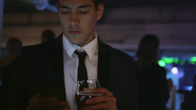 Gut-gekleidete-junge-Mann-in-einem-Nachtclub-hält-einen-Drink-und-SMS