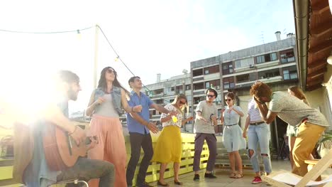 Glückliche-Leute-tanzen-und-spielen-Gitarre-auf-der-Dachparty-am-sonnigen-Tag