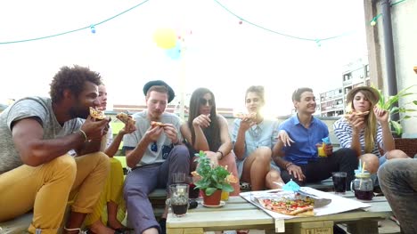 Jóvenes-sentados-alrededor-de-la-mesa-y-comer-pizza-en-la-terraza-de-la-azotea
