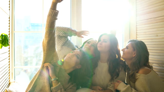 cuatro-hermosas-chicas-disparan-selfie-sentado-en-la-ventana.-Novias-teniendo-diversión-y-risa-en-dormitorio