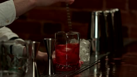 Professional-bartender-at-work-in-bar-mixing-ice-and-liquor-in-glass-for-drink