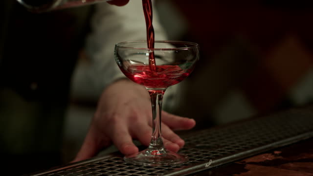 Barman-gießt-roten-Alkohol-und-bereitet-kosmopolitisch-ins-Champagnerglas