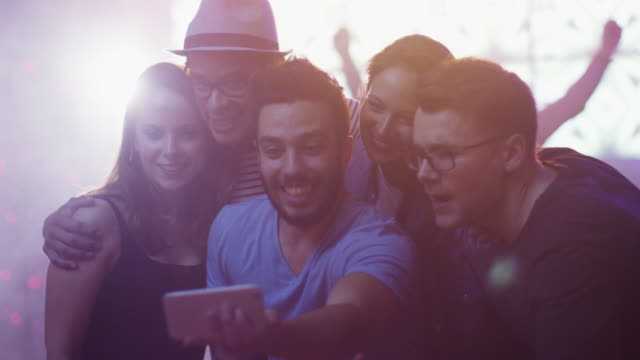 Group-of-Happy-Smiling-Friends-doing-Selfies-with-Mobile-Phone-on-Party.
