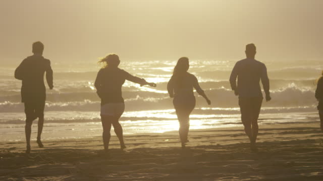 Friends-running-to-ocean-at-sunset-in-slow-motion