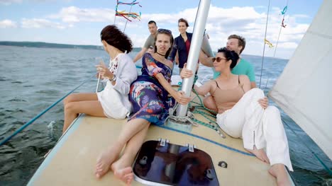A-company-of-friends-ride-on-a-yacht-on-the-high-seas-or-the-ocean,-buddies-sit-on-deck-and-enjoy-a-light-wind-that-blows-their-hair-and-clothes