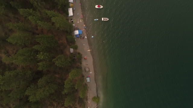 Drone-Over-Lake-Beach-Camp-Site-with-Boats-and-Tents