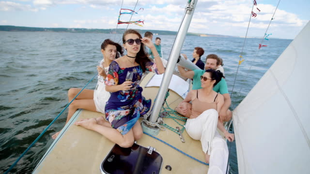 jóvenes-son-paseos-en-barco-sobre-el-mar-y-beber-champagne-en-día-de-verano-en-clima-ventoso,-sentado-cerca-de-mástil