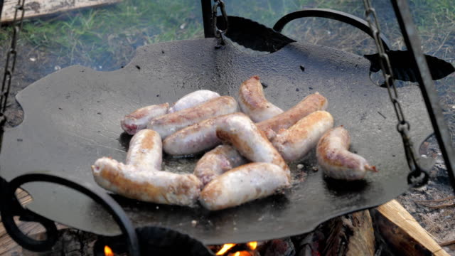 Flipped-Tasty-Juicy-Sausages-Fry-In-a-Frying-Pan-Suspended-Over-Fire,-Barbecue